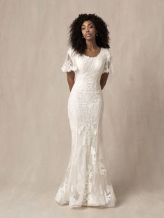 a woman in a white wedding dress with an open back and short sleeves, standing against a