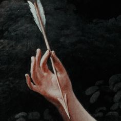 a hand holding a feather on top of a rock