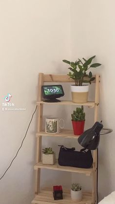 a wooden shelf with plants and purses sitting on top of it next to a bed