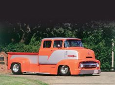 an orange and white truck parked in front of a brick wall with trees behind it