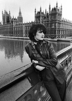 black and white photograph of woman leaning on wall next to water with big ben in the background