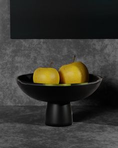 two pears and one apple in a black bowl on a gray table with grey background