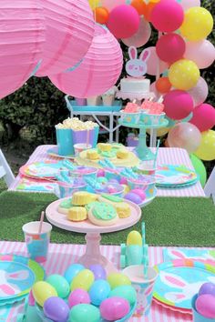 a table topped with lots of colorful desserts and balloons on top of grass covered ground