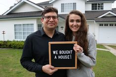 a man and woman standing in front of a house holding a sign that says we bought a house