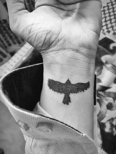 a black and white photo of a person with a bird tattoo on their left wrist