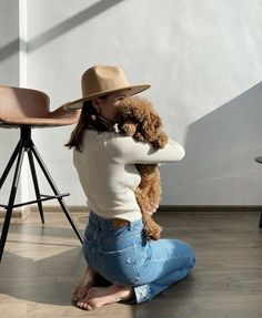 a woman sitting on the floor with her dog wearing a hat and holding it up to her face