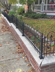 a black iron fence on the side of a sidewalk in front of a brick house