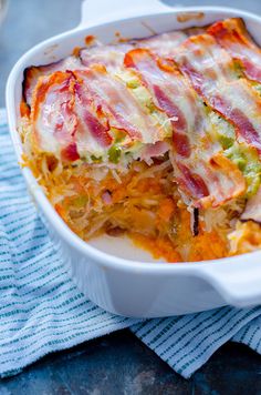 a casserole dish with bacon, cheese and other toppings on a blue towel