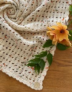 a crocheted blanket with a yellow flower on the end and green leaves around it