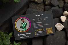 a black business card sitting on top of rocks next to some green plants and stones