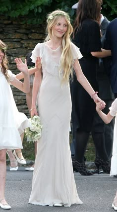 a mother and daughter holding hands while walking down the street with other people behind them