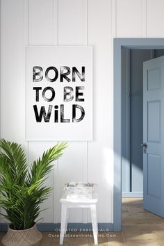 a white chair sitting next to a green plant in front of a wall with a sign that says born to be wild