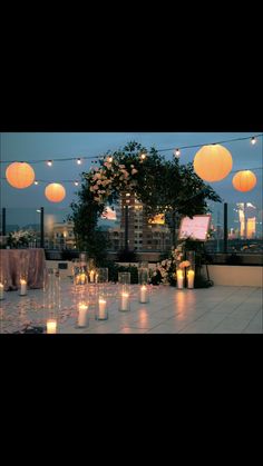 an outdoor event with candles and paper lanterns hanging from the ceiling, on top of a roof