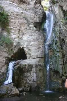 a man standing next to a waterfall in the middle of a rocky mountain side area