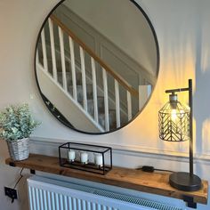 a round mirror hanging on the wall above a radiator with candles and a potted plant