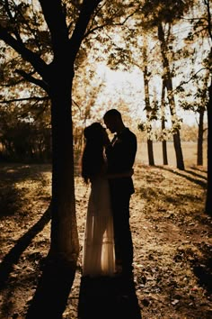 a man and woman standing next to each other under a tree in the sun light