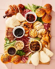 an assortment of meats, bread and sauces on a cutting board with buns