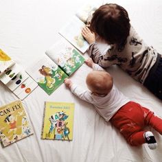 a baby is laying on the bed reading a book with other children's books