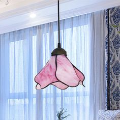 a pink lamp hanging from a ceiling in a living room next to a window with curtains