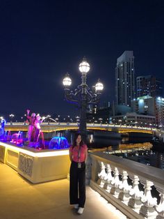 a woman standing on the edge of a walkway next to a light sculpture at night