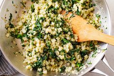 a wooden spoon in a pan filled with rice and spinach salad ingredients on a table