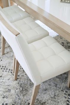 a dining room table with two white chairs and a rug on the floor in front of it