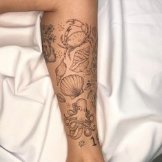 a woman's leg with tattoos on it and seashells in the background