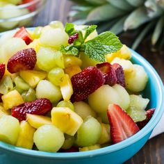 a blue bowl filled with fruit salad on top of a wooden table next to pineapples