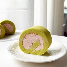 a green and pink cake roll on a white plate next to another one in the background