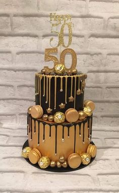 a three tiered cake decorated with gold and black icing, topped with chocolate drips