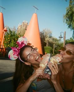 two women eating donuts in front of an orange cone - shaped building at disneyland