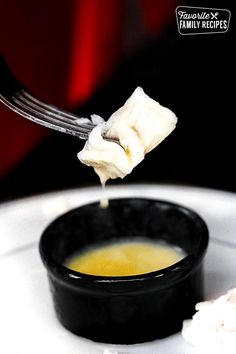 a fork with some food in it on a white plate next to a black bowl