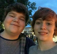 two young boys standing next to each other in front of a building at dusk with their eyes closed