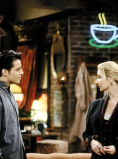 a man and woman standing next to each other in front of a coffee shop sign