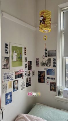 a bed sitting under a window next to a wall with pictures on the walls and a lamp hanging above it