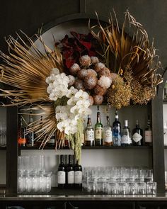 a bar with bottles and glasses on the shelves filled with liquor, flowers and plants