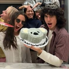 a group of people holding up a cake with a teddy bear on it in front of them