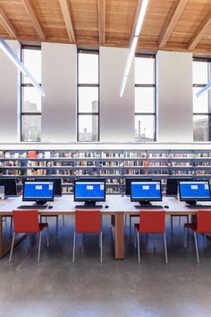 several laptops sitting on tables in a library with bookshelves full of books