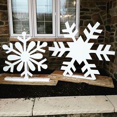 two snowflakes sitting on top of a piece of wood in front of a window