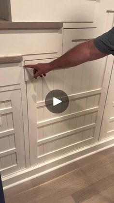 a man standing in front of a white kitchen cabinet door and pointing to the drawer