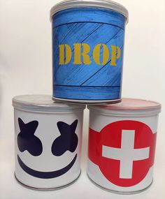 three tins with painted faces and the word drop on them are stacked next to each other