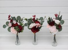 three vases with flowers and greenery in them