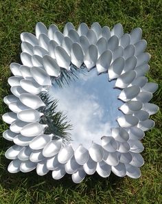 a large metal flower shaped mirror sitting on top of a grass covered field next to a pine tree