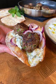 a hand holding a sandwich with meatballs and onions on it next to some pita bread