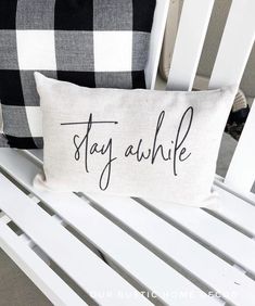 a pillow that says stay awhile sitting on a white bench with black and white pillows