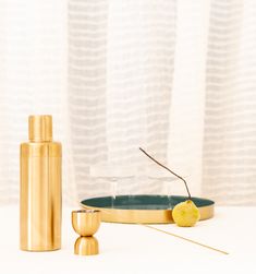 a table topped with a gold plate and two glasses next to a bottle filled with liquid