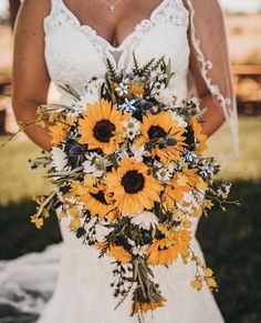 a bride holding a bouquet of sunflowers and greenery on her wedding day