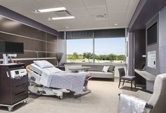 an empty hospital room with medical equipment in the foreground and large windows to the outside