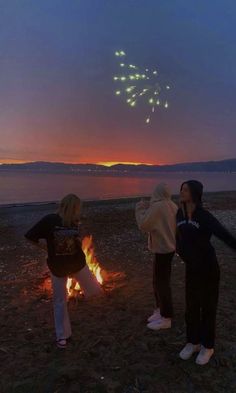 three people standing in front of a fire on the beach at night with fireworks coming from them