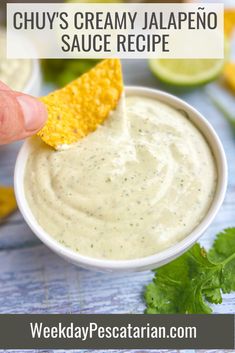 a hand dipping a tortilla chip into a white sauce